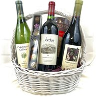 White basket with three bottles of wine, chocolates, and a canister of snacks