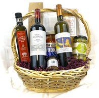 Tan basket filled with two bottles of Italian wine, pasta sauce, olives, olive oil, pasta, and snacks