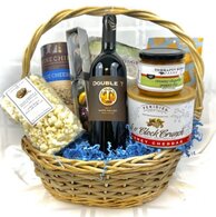 tan basket filled with one bottle of wine and lots of snack foods, including popcorn, dips, snack mix, chocolates, potato chips, peanut brittle.