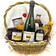 tan basket filled with a bottle of sparkling wine, jam, pancake mix, honey, syrup, small cookies and bloody mary mix.